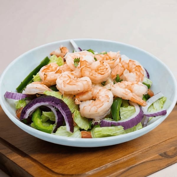 Shrimp salad with lettuce, red onion, and green peppers in a light blue bowl on a wooden board.