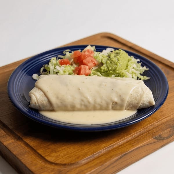 A large burrito covered in white cheese sauce, served with shredded lettuce, diced tomatoes, and guacamole.