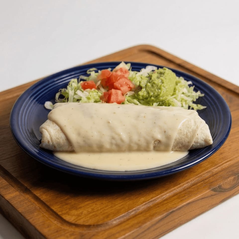A large burrito covered in white cheese sauce, served with shredded lettuce, diced tomatoes, and guacamole.